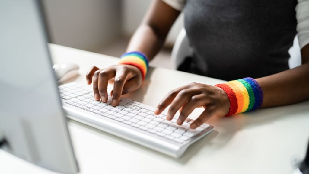 A person focused on crafting a mental health website design types away at a keyboard, vibrant rainbow-striped wristbands adorning their wrists, as they sit at a desk in front of a computer.